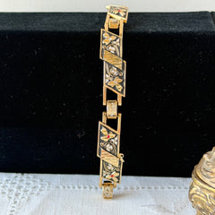 Vintage Spanish damascene gold‑tone bracelet with black enamel floral links, silver inlay, and red rhinestone accents, shown in various angles highlighting its 1960s Toledo craftsmanship and slide clasp with safety chain.