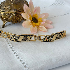 Vintage Spanish damascene gold‑tone bracelet with black enamel floral links, silver inlay, and red rhinestone accents, shown in various angles highlighting its 1960s Toledo craftsmanship and slide clasp with safety chain.