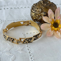 Vintage Spanish damascene gold‑tone bracelet with black enamel floral links, silver inlay, and red rhinestone accents, shown in various angles highlighting its 1960s Toledo craftsmanship and slide clasp with safety chain.