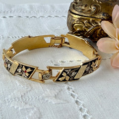 Vintage Spanish damascene gold‑tone bracelet with black enamel floral links, silver inlay, and red rhinestone accents, shown in various angles highlighting its 1960s Toledo craftsmanship and slide clasp with safety chain.
