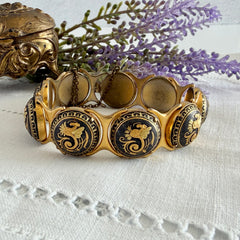 Vintage Spanish damascene bracelet with black enamel and gold‑tone salamander motifs in round links, shown on a white embroidered surface with decorative props.