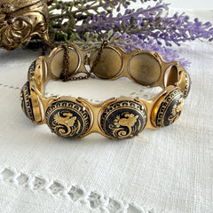 Vintage Spanish damascene bracelet with black enamel and gold‑tone salamander motifs in round links, shown on a white embroidered surface with decorative props.