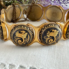 Vintage Spanish damascene bracelet with black enamel and gold‑tone salamander motifs in round links, shown on a white embroidered surface with decorative props.