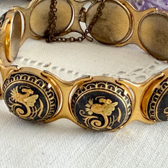 Vintage Spanish damascene bracelet with black enamel and gold‑tone salamander motifs in round links, shown on a white embroidered surface with decorative props.