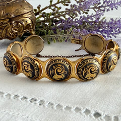 Vintage Spanish damascene bracelet with black enamel and gold‑tone salamander motifs in round links, shown on a white embroidered surface with decorative props.