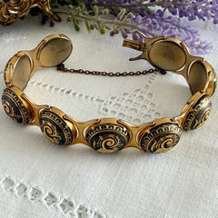 Vintage Spanish damascene bracelet with black enamel and gold‑tone salamander motifs in round links, shown on a white embroidered surface with decorative props.