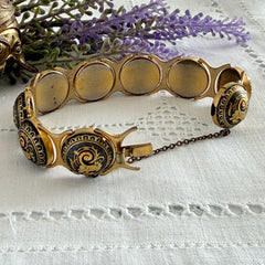 Vintage Spanish damascene bracelet with black enamel and gold‑tone salamander motifs in round links, shown on a white embroidered surface with decorative props.