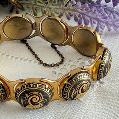 Vintage Spanish damascene bracelet with black enamel and gold‑tone salamander motifs in round links, shown on a white embroidered surface with decorative props.