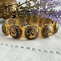 Vintage Spanish damascene bracelet with black enamel and gold‑tone salamander motifs in round links, shown on a white embroidered surface with decorative props.