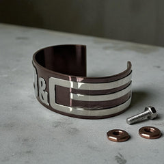 Dolce & Gabbana men's stainless steel cuff bracelet with a brown finish and raised silver-tone logo plaque; modern designer accessory with bold branding and sculptural detail.