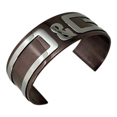 Dolce & Gabbana men's stainless steel cuff bracelet with a brown finish and raised silver-tone logo plaque; modern designer accessory with bold branding and sculptural detail.