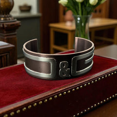 Dolce & Gabbana men's stainless steel cuff bracelet with a brown finish and raised silver-tone logo plaque; modern designer accessory with bold branding and sculptural detail.
