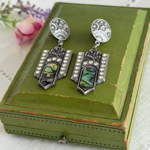 Vintage Duri Art Deco‑style abalone and rhinestone dangle post earrings with ornate floral metalwork and iridescent inlay, shown on display and vintage box.