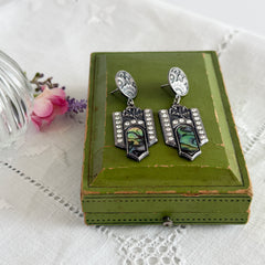 Vintage Duri Art Deco‑style abalone and rhinestone dangle post earrings with ornate floral metalwork and iridescent inlay, shown on display and vintage box.