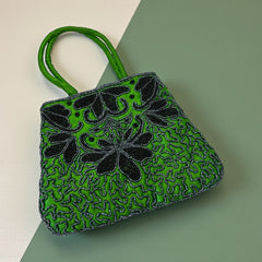 Vintage 1990s emerald green satin evening bag with handsewn black and hematite glass bead floral motifs, dual green handles, and optional crossbody cord, photographed to show craftsmanship, texture, and convertible styling.