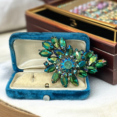 Vintage 1950s brooch featuring layered AB emerald rhinestones in marquise and chaton cuts, set in silver tone metal with a central dog tooth prong setting; photographed to highlight sparkle, craftsmanship, and mid-century design.