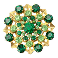 Vintage 1950s gold tone brooch with a ruffled sunburst design, featuring concentric rings of emerald and peridot rhinestones and a large green center stone; bold mid-century costume jewelry with layered sparkle and sculptural detail.