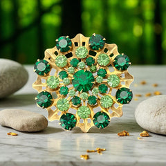Vintage 1950s gold tone brooch with a ruffled sunburst design, featuring concentric rings of emerald and peridot rhinestones and a large green center stone; bold mid-century costume jewelry with layered sparkle and sculptural detail.