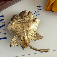 Vintage 1997 Graziano ‘England’s Rose’ brooch with light pink enamel‑painted petals, light green enamel‑painted leaves, clear rhinestones, and a gold‑tone stem, signed on the back.