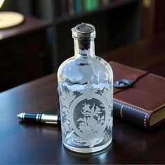 Set of two vintage etched glass apothecary bottles with frosted floral designs and cork stoppers topped with metal rings, photographed in natural light.