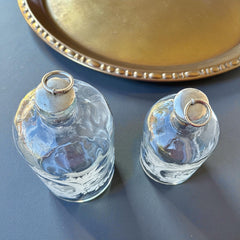 Set of two vintage etched glass apothecary bottles with frosted floral designs and cork stoppers topped with metal rings, photographed in natural light.