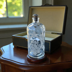 Set of two vintage etched glass apothecary bottles with frosted floral designs and cork stoppers topped with metal rings, photographed in natural light.