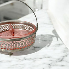 Vintage Farberware relish dish featuring pink Depression glass in a divided three-section design, set in a silver-tone openwork metal basket with arched handle and pedestal base; photographed in soft light to highlight its rosy hue and Art Deco detailing.