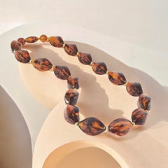1950s vintage faux amber necklace featuring cognac-colored twisted plastic beads with gold-tone accents and a matching barrel clasp. A shiny, elegant piece in very good vintage condition, perfect for sustainable and eco-conscious fashion.
