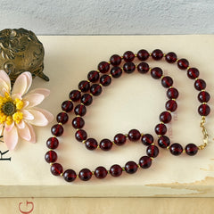 Vintage cherry amber acrylic bead necklace with gold tone spacers and clasp displayed on neutral background.