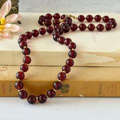 Vintage cherry amber acrylic bead necklace with gold tone spacers and clasp displayed on neutral background.