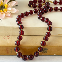 Vintage cherry amber acrylic bead necklace with gold tone spacers and clasp displayed on neutral background.