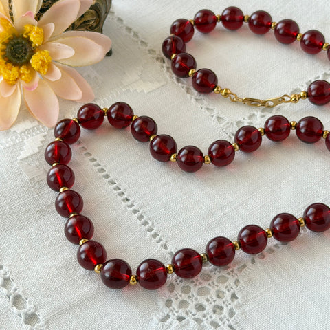 Vintage cherry amber acrylic bead necklace with gold tone spacers and clasp displayed on neutral background.