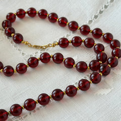 Vintage cherry amber acrylic bead necklace with gold tone spacers and clasp displayed on neutral background.
