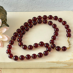 Vintage cherry amber acrylic bead necklace with gold tone spacers and clasp displayed on neutral background.