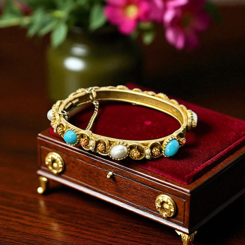 Vintage 1950s gold-tone hinged bangle bracelet with faux turquoise, coral, and pearl cabochons, shown on red velvet display. Features textured finish, safety chain, and romantic Victorian Revival design.