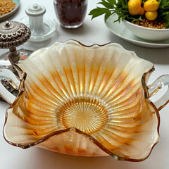Vintage Fenton marigold carnival glass dish with stippled rays pattern, featuring a ruffled scalloped edge and clear double handles; warm amber iridescence with visible air bubbles 