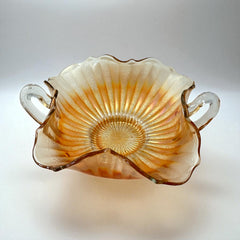 Vintage Fenton marigold carnival glass dish with stippled rays pattern, featuring a ruffled scalloped edge and clear double handles; warm amber iridescence with visible air bubbles 