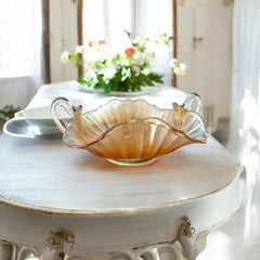 Vintage Fenton marigold carnival glass dish with stippled rays pattern, featuring a ruffled scalloped edge and clear double handles; warm amber iridescence with visible air bubbles 