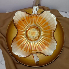 Vintage Fenton marigold carnival glass dish with stippled rays pattern, featuring a ruffled scalloped edge and clear double handles; warm amber iridescence with visible air bubbles 