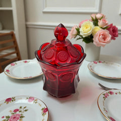 Vintage Fostoria Ruby Red Coin Glass candy dish with lid, featuring embossed coin medallions and a pointed finial; shown in rich red pressed glass with original Fostoria sticker, styled to highlight its collectible elegance and mid-century provenance.