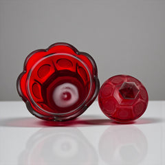 Vintage Fostoria Ruby Red Coin Glass candy dish with lid, featuring embossed coin medallions and a pointed finial; shown in rich red pressed glass with original Fostoria sticker, styled to highlight its collectible elegance and mid-century provenance.