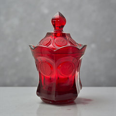 Vintage Fostoria Ruby Red Coin Glass candy dish with lid, featuring embossed coin medallions and a pointed finial; shown in rich red pressed glass with original Fostoria sticker, styled to highlight its collectible elegance and mid-century provenance.