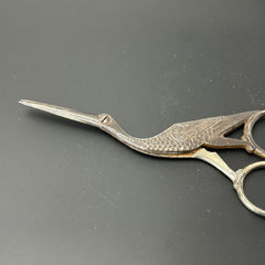 Antique French stork-shaped embroidery scissors from the late 1800s to early 1900s. Crafted with intricate details, the silver-tone finish shows charming wear, revealing darker metal and hints of faded gold-tone accents on the stork’s body when opened. A collectible and decorative piece embodying timeless craftsmanship and vintage elegance.