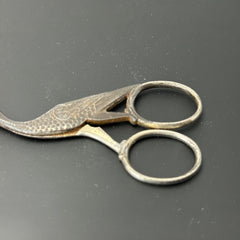Antique French stork-shaped embroidery scissors from the late 1800s to early 1900s. Crafted with intricate details, the silver-tone finish shows charming wear, revealing darker metal and hints of faded gold-tone accents on the stork’s body when opened. A collectible and decorative piece embodying timeless craftsmanship and vintage elegance.