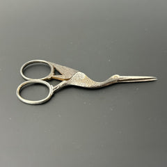 Antique French stork-shaped embroidery scissors from the late 1800s to early 1900s. Crafted with intricate details, the silver-tone finish shows charming wear, revealing darker metal and hints of faded gold-tone accents on the stork’s body when opened. A collectible and decorative piece embodying timeless craftsmanship and vintage elegance.