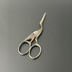Antique French stork-shaped embroidery scissors from the late 1800s to early 1900s. Crafted with intricate details, the silver-tone finish shows charming wear, revealing darker metal and hints of faded gold-tone accents on the stork’s body when opened. A collectible and decorative piece embodying timeless craftsmanship and vintage elegance.