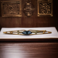 Vintage French Art Deco bar brooch with blue marquise rhinestone, gold-plated metal, and silver-tone leaf accents