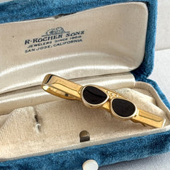 Vintage French gold‑tone tie clip with black enamel sunglasses motif from the 1980s.