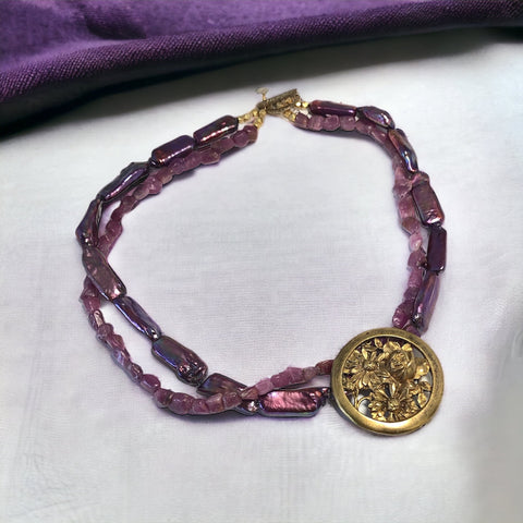 Necklace with vintage 1930s French gold‑tone floral brooch pendant on two strands of purple‑pink dyed stick pearls and rough rubies, shown from multiple angles.