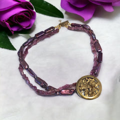 Necklace with vintage 1930s French gold‑tone floral brooch pendant on two strands of purple‑pink dyed stick pearls and rough rubies, shown from multiple angles.